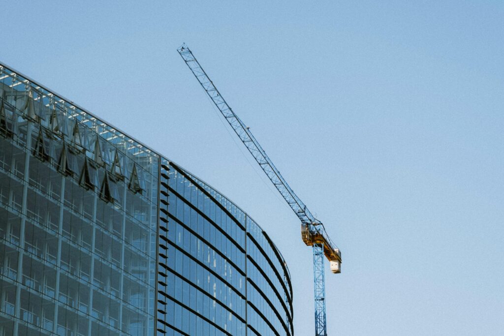 Contemporary glass building under construction with a visible crane against a clear blue sky.